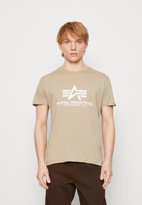 Tricou din bumbac bej cu mâneci scurte, având un imprimeu grafic alb cu accente geometrice pe față.