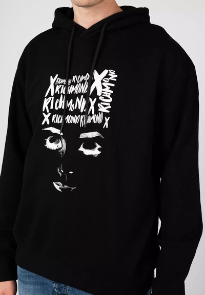 Felpa nera con cappuccio caratterizzata da una grande grafica bianca che presenta un viso e del testo sovrapposto. Il materiale sembra liscio, con cappuccio regolabile e polsini a coste.