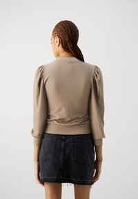 Maglione beige a coste con maniche a palloncino, caratterizzato da un colletto alto e una vita aderente, abbinato a una mini gonna in denim scuro.