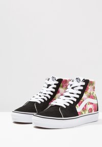 Baskets montantes avec un extérieur en daim noir, des lacets blancs et un motif floral en rose et vert sur les côtés. Semelle en caoutchouc blanche.