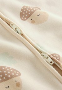 Tissu de pyjama avec un fond beige clair et des illustrations colorées de champignons, fermeture éclair, et une sensation douce et texturée.
