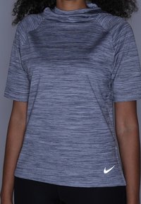 Top deportivo gris de manga corta con un patrón texturizado, un cuello alto y un pequeño logo de Nike blanco en el dobladillo inferior.