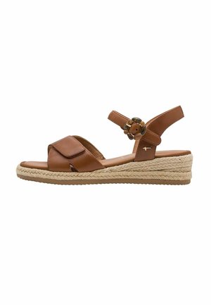 Brun læder kilehæl sandal med flettet jutesål, justerbar anklerem og dekorativ rund spænde på hvid baggrund.