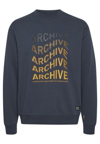 Sudadera azul navy con cuello redondo, que presenta el texto "ARCHIVE" en diferentes tamaños y colores metálicos oro, gris y negro.