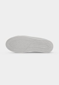 Semelle blanche de chaussure de sport avec motif géométrique et texte "Tommy Hilfiger" embossé près du talon, présenté sur fond blanc.