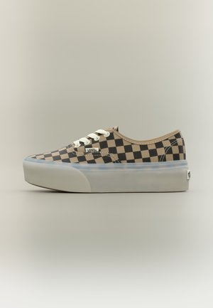 Zapatilla baja Vans con patrón de tablero de ajedrez beige y negro, cordones blancos y suela gruesa translúcida sobre fondo neutro.