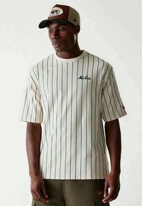 Wit gestreept T-shirt met korte mouwen, met marineblauwe verticale lijnen en een klein groen "New Era" logo op de borst. Casual pasvorm.