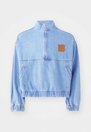 Light blue denim cropped jacket with a high collar, half-zip closure, and elasticized cuffs. Features a brown logo patch on the chest.