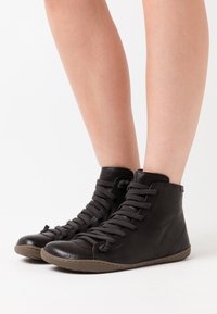 Pantofi sport negri, tip bocanc, din piele, având vârful rotund, șireturi groase și o suprafață texturată cu talpă din cauciuc bej deschis.