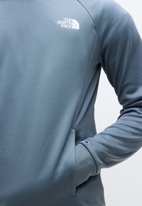 Φωτεινό γαλάζιο φούτερ κατασκευασμένο από υφασμάτινη ύφανση. Διαθέτει μακριά μανίκια, στρογγυλή λαιμόκοψη και ένα μικρό λευκό λογότυπο στο πάνω αριστερό μέρος.