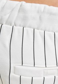Tissu blanc avec des rayures horizontales noires. Taille élastique et un petit détail de poche. Texture douce avec des coutures visibles.