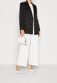 Blazer a strisce zebrate nere con taglio sartoriale, pantaloni oversize bianchi, scarpe con tacco alto bianche e una piccola borsa bianca.