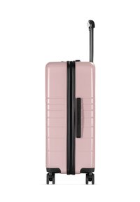 Rosa Hartschalenkoffer mit vertikal geriffeltem Design, schwarzem Reißverschluss und Griff. Vier Räder für Mobilität, schlanke und kompakte Form.