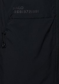 Schwarzer Stoff mit Reißverschluss rechts und schwarzem Reißverschlussanhänger links, Text "HALO" und Zahlen "96819721981" in der Nähe der oberen Mitte gedruckt.