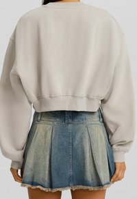 Felpa beige Cropped con maniche oversize, abbinata a una gonna in denim azzurro chiaro con pieghe e orlo sfilacciato.