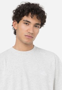 Grå bomulls t-shirt med rund hals och korta ärmar. Har en liten vit logotyp på vänster bröst. Mjuk textur, avslappnad passform.