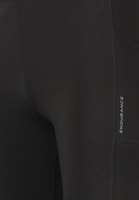 Leggings deportivas negros hechos de tela elástica, con un bolsillo lateral y la palabra "ENDURANCE" impresa en blanco. Textura suave, diseño ajustado.