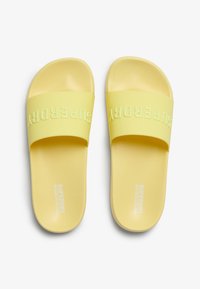 Yellow slide sandals made of soft material featuring a wide strap embossed with "SUPERDRY." Textured footbed and smooth sole.