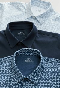 Tres camisas de cuello en diferentes tonos de azul. Una de color azul marino sólido, una azul claro con un patrón geométrico y una azul oscuro con un patrón de diamantes.