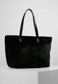 Černá kabelka z umělé kožešiny s hladkými koženými uchy, obdélníkový tvar, měkká textura a jemný povrch pro dodání hloubky.