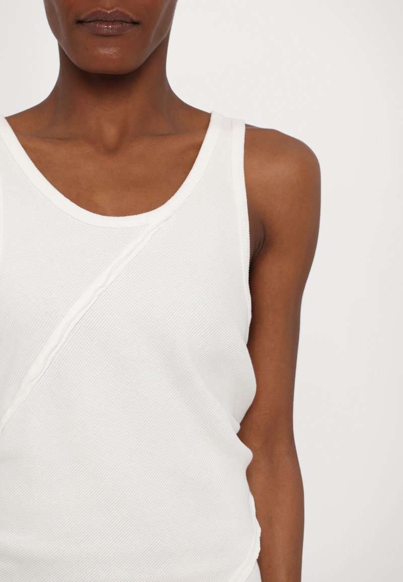 Witte mouwloze tanktop met een ribbelstructuur, ronde halslijn en diagonale naaddetails aan de voorkant.