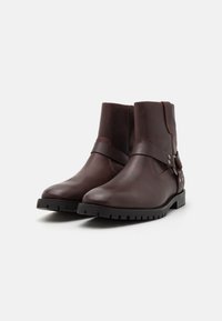 Brown leather ankle boots with a smooth finish, feature a wide strap and decorative buttons, and have a textured rubber sole for traction.