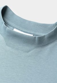 Helles blaues, kurzärmliges Shirt mit einem gerippten Rundhalsausschnitt und strukturiertem Stoff. Verfügt über ein dezentes Nahtdetail in der Nähe des Halsausschnitts.