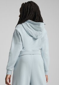 Himmelblaues, kurzes Hoodie aus weichem Material, ausgestattet mit einer Kapuze, gerippten Bündchen und einem nahtlosen Design mit minimalen Nähten.