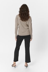 Beige top met lange mouwen, gecombineerd met zwarte straight-leg broek. De top heeft een zachte textuur, en de broek heeft een gladde afwerking met minimale details.