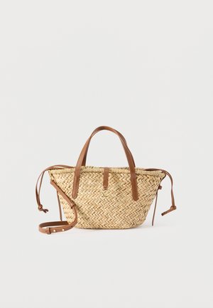 Πλεκτή τσάντα χειρός από ψάθα με καφέ δερμάτινες λαβές, ρυθμιζόμενο ιμάντα ώμου και λεπτομέρειες με κορδόνια στις πλευρές, σε λευκό φόντο.