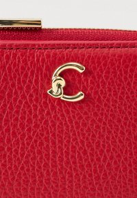 Červená texturovaná kožená peněženka se zlatým zipem a vzájemně propleteným zlatým kovovým emblémem připomínajícím dvě stylizované písmena C.