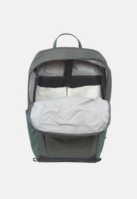 Der Innenraum eines grünen Rucksacks mit einem grauen Futter, verstellbaren Schulterriemen und mehreren Fächern zur Organisation.
