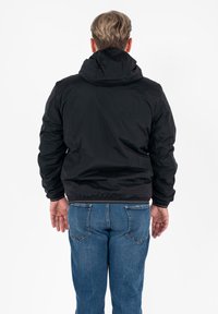 Giacca nera con cappuccio, dal finish liscio e con polsini elasticizzati, abbinata a jeans in denim blu. L'outfit presenta una vestibilità e un taglio casual.