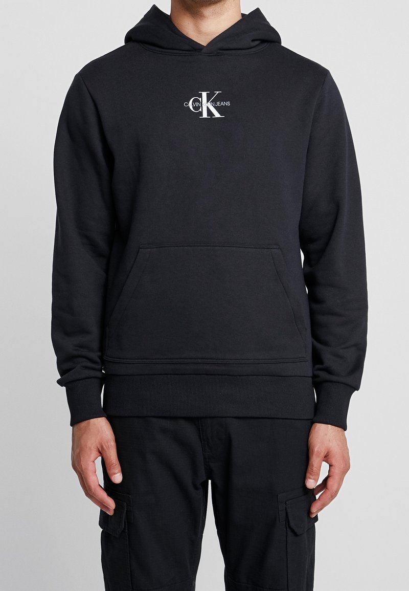 Sudadera negra con capucha, bolsillo frontal y puños y dobladillo de canalé. Cuenta con una impresión de logotipo blanco en el pecho. Fabricada con tejido suave.