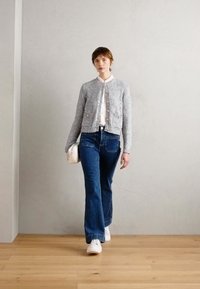 Gray textured cardigan with round neckline, white shirt, flared blue jeans, and white sneakers. Model carries a small cream handbag.