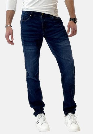 Jeans in denim blu scuro con un design aderente, dettagli di sbiadimento delicati, cinque tasche e bottone dorato, abbinati a sneakers bianche.