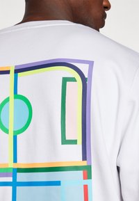 T-shirt en coton blanc avec un imprimé géométrique coloré en bleu, vert, rose, violet et orange au dos. Manches courtes, col rond.