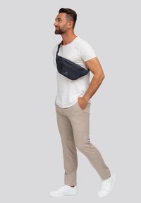 Marsupio blu navy realizzato in materiale resistente, dotato di due scomparti con zip e una tracolla regolabile. Indossato sopra la spalla.
