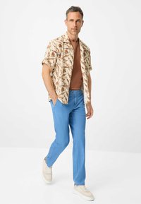 Camicetta a maniche corte color crema con stampa floreale marrone, t-shirt marrone, pantaloni azzurri chiari e sneakers beige, creando un outfit casual.