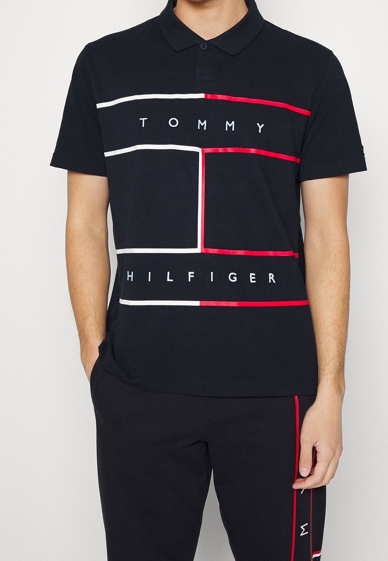 Mustapaita, jossa on punaisia ja valkoisia vaakaraitoja sekä "TOMMY HILFIGER" -teksti. Lyhyet hihat, kauluksellinen kaula-aukko, puuvillamateriaali.