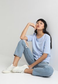 Blå og hvidstribet T-shirt, afslappet pasform med rund halsudskæring; parret med lysblå slidte jeans og hvide sneakers.