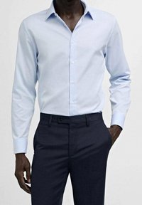 Camicia azzurra a maniche lunghe con colletto a punta, apertura con bottoni e tessuto morbido, abbinata a pantaloni scuri.