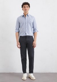 Light blue striped button-up shirt, dark pants, and white sneakers. The shirt has long sleeves and a subtle logo on the chest.