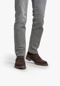 Braune Wildleder-Stiefeletten mit strukturiertem Finish, Schnürdesign und rutschfester Gummisohle. Tragen Sie dazu hellgraue, taillierte Jeans.