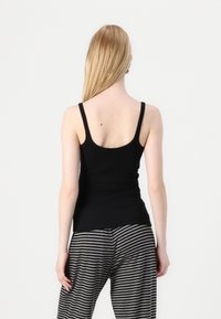 Svart tank topp med tynne stropper, tettsittende design, myk tekstur, kombinert med grå og svarte stripete bukser. Sett fra baksiden.