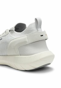 Biały sneaker z teksturowaną dzianinową cholewką, zamszowym paskiem na pięcie, pętelką do ściągania i grubą, żebrowaną podeszwą, widoczny z tyłu pod kątem.