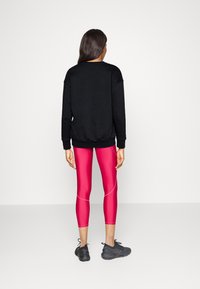 Black long-sleeve sweatshirt paired with fitted pink leggings featuring contrasting seams, and black athletic shoes. Simple, sporty look.