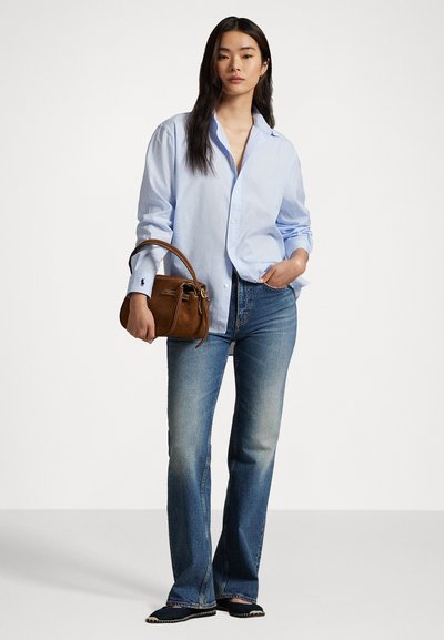 Chemise bleu clair à col boutonné, jeans bleus, sac à main marron, chaussures noires avec coutures blanches, avec une coupe décontractée et un style casual.