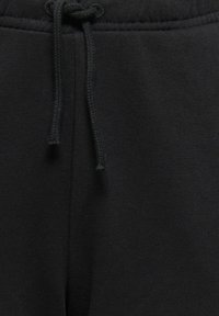 Close-up of black fabric pants with visible drawstring tied at the waistband, showing texture and stitching details.