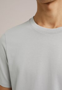 Šviesiai pilkas trumpų rankovių marškinėliai, pagaminti iš minkštos medvilnės, su klasikiniu apvaliu kaklu ir lygiu paviršiumi. Be matomų raštų.